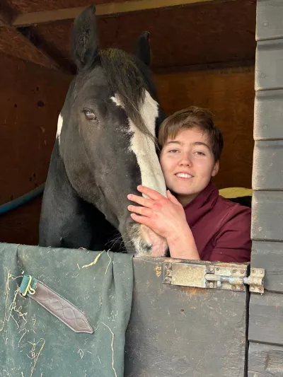 A woman holds a horse's face from a stable.
