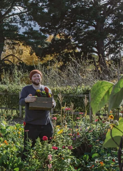 A young man carries a plant through a garden.