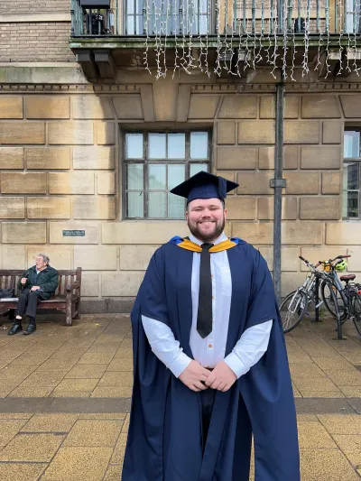 A young man stands proudly in his graduation garb.