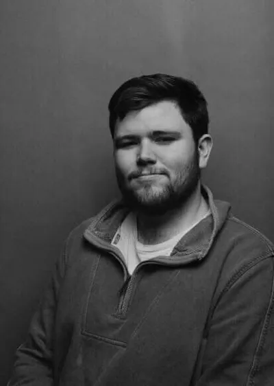 A young man smiles for a black and white portrait.