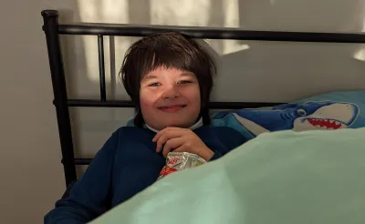 A young boy smiles from his bed.