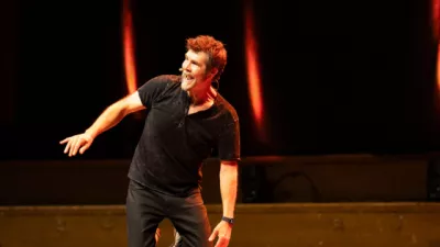 Rhod Gilbert performs stand-up on a dark stage.