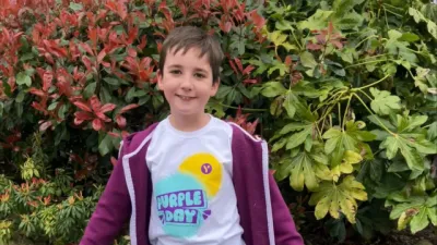 A young boy, tent, poses in a Purple Day Young Epilepsy t-shirt.