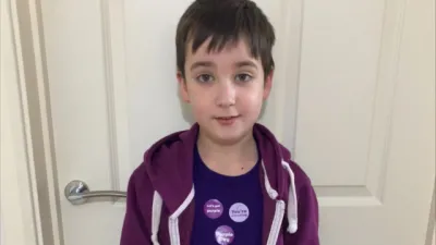 A young boy, Tate, wears three Purple Day badges on a purple t-shirt.