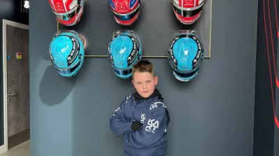 A boy folds his arms, standing in front of a wall of motocross racing helmets.