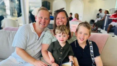 A mother, father, and their two boys smile to camera.
