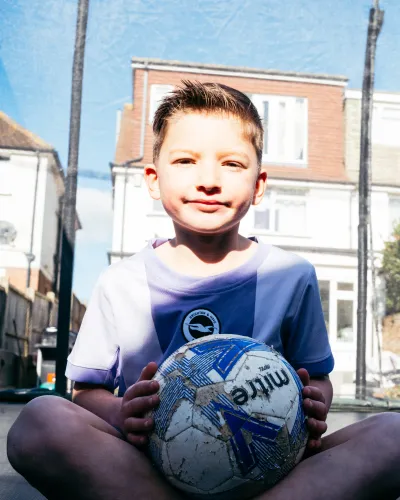 A young boy holds a football as he sits on a trampoline.