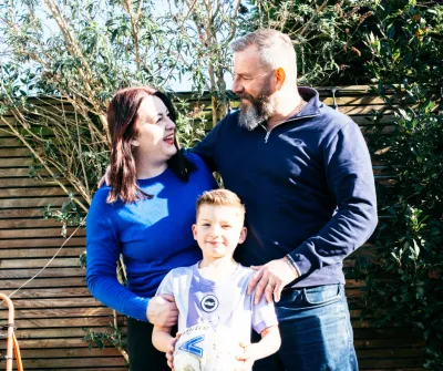 A young boy holds a football, stood between his mother and father.