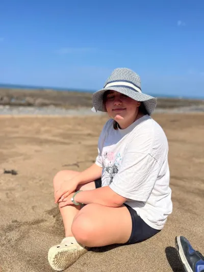 A young woman sits on a sandy beach.