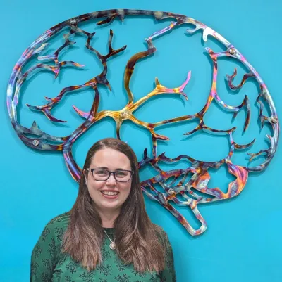 A woman stands in front of a blue wall decorated with a sculpture of a brain.