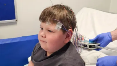 A boy sits in a hospital bed with an EEG.