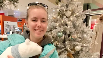 A young woman holds a polar bear stuffie besides a Christmas tree.