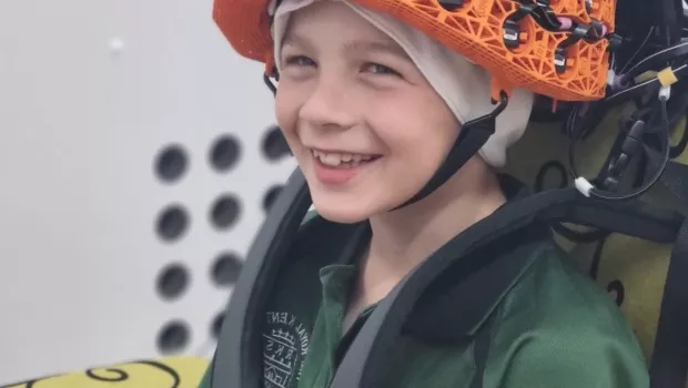 Young boy smiles at camera wearing an orange OPM-MEG helmet