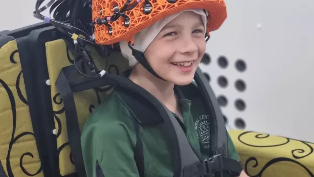 Young boy smiles at camera wearing an orange OPM-MEG helmet