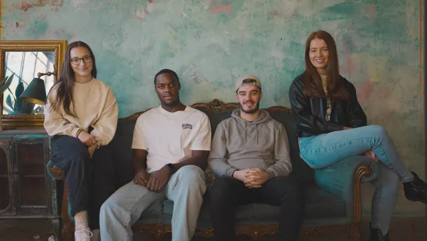 Four young people, two women and two men, sit on a sofa smiling at the camera