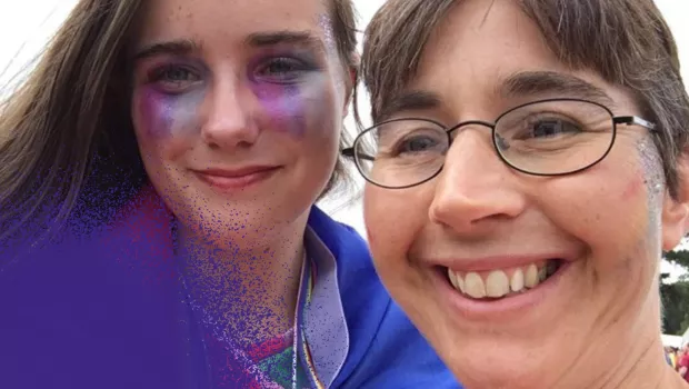 Selfie of one young woman and one older smiling at the camera.  Younger one has purple make up on.