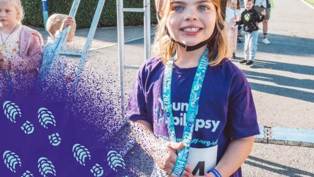 Photograpgh of young girl at the end of a race.  she is earing a purple t-shirt and runners media.  Young Epilepsy purple spray paint is in the bottom left hand corner with blue footprints placed across its   