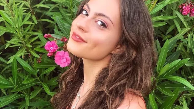 Olivia, a young woman, smiles in a selfie before a flowery bush.