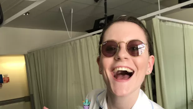 A nurse wearing sunglasses smiles widely to the camera while working on a ward.