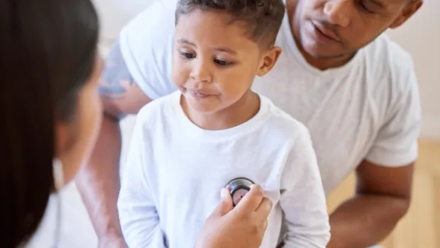 A young boy is being checked over by a healthcare professional while a parent watches over.