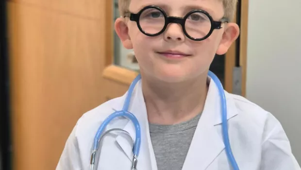 A child is wearing character glasses and stethoscope with a doctor's coat.