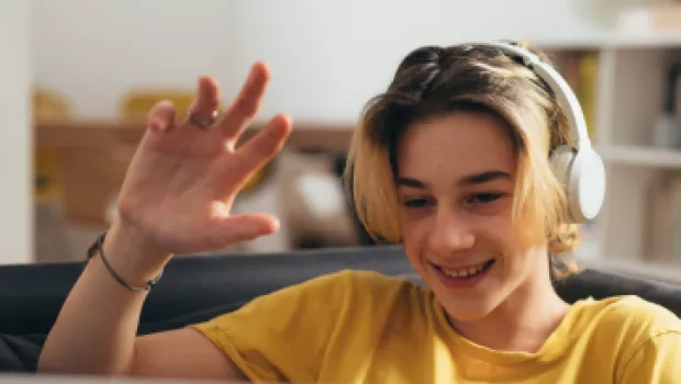 A teenage boy smiles and waves on a video call.