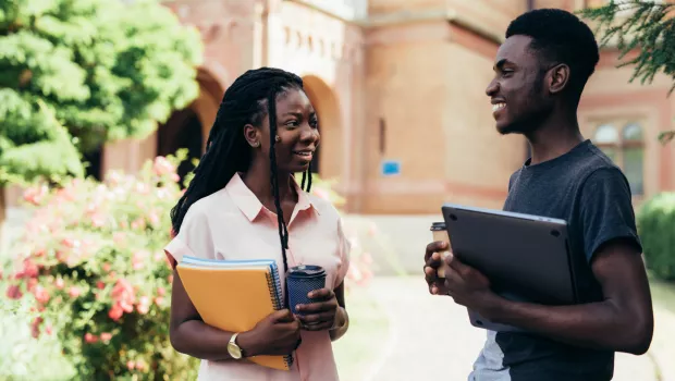 Young male and female adults chat with notebook and coffee in hand.