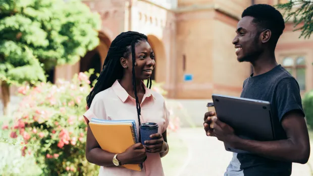 Young male and female adults chat with notebook and coffee in hand.