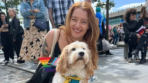 A young woman poses with her dog at a Pride parade.