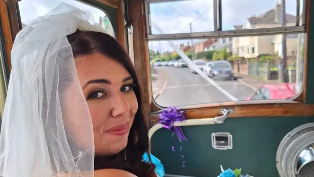 Laura, a young woman, smiles in a wedding dress from a vehicle.