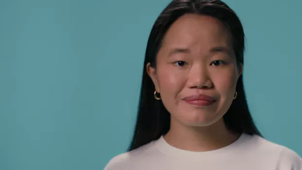 A young Asian girl stands against a blue backdrop wearing a white t-shirt