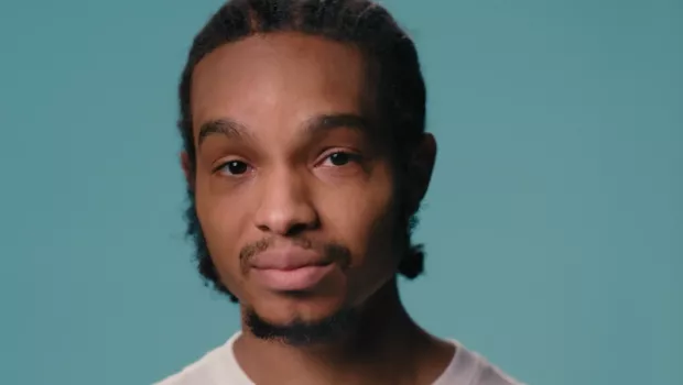 A young black boy stands against a blue backdrop wearing a white t-shirt