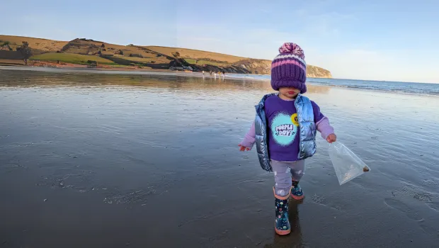 A cute child wearing a Young Epilepsy Purple Day t-shirt walks on the beach with a hat covering face.