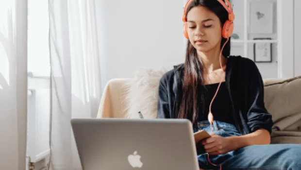 Teenage girl wearing headphones looking at laptop for an online video call.