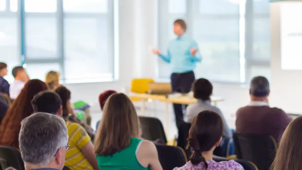 A teacher stands in front of a classroom presenting information.