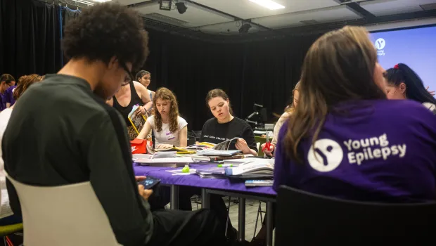 A group of young people make make collages at a table in Young Epilepsy clothing.