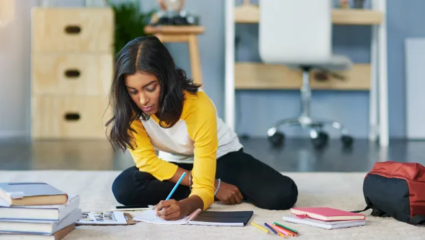 A teenager, sat on the floor, writes notes down in a diary.