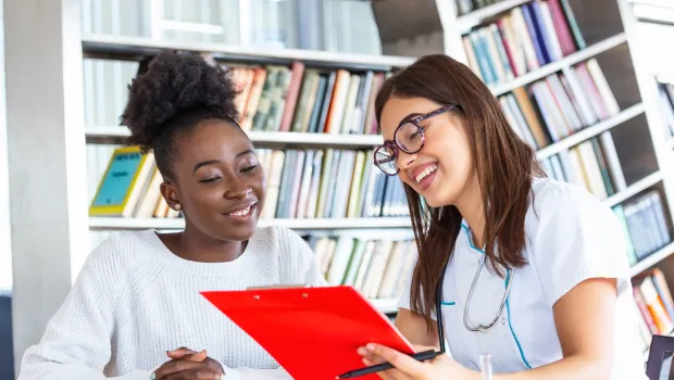 A teenager and doctor smile as they look at something on a clipboard in an office.