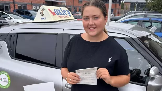 A young woman stands by a learner car, showing that she passed her driver's license.