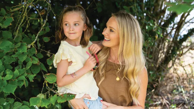 A mother holds her daughter outside, both smiling.