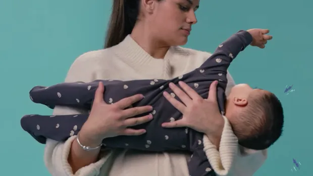 A mother holds her infant against a blue backdrop.