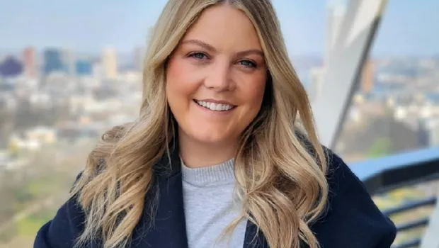 A young woman smiles from a viewpoint over a city.