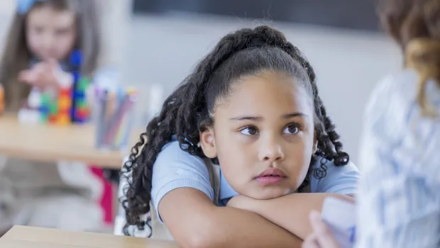 A young girl sits thoughtfully at a desk.
