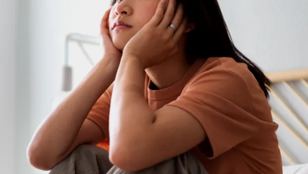A young woman sits thoughtfully on a bed.