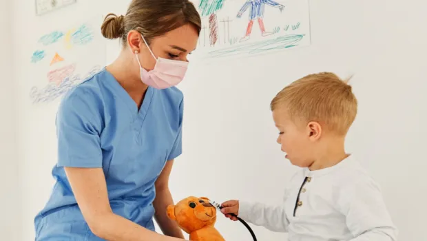 A nurse plays with a young patient and teddy bear.