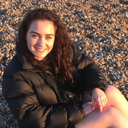 photograpgh of young woman on a pebble beach, smiling at the camera with the evening sun on her face 