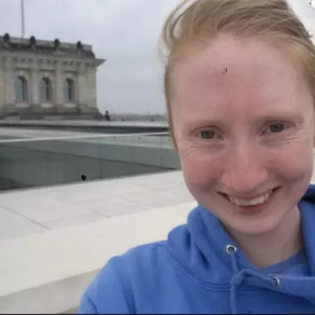 Selfie of young woman smiling in the wind with building in the background.