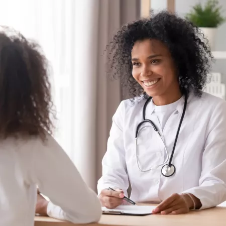 A medical professional smiles at a younger patient during a consultation.