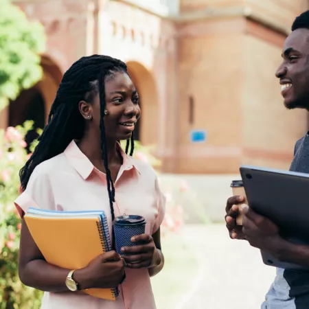 Young male and female adults chat with notebook and coffee in hand.