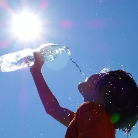 young child pours water from a bottle in the hot sun
